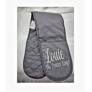 May include: Gray oven mitts with quilted fabric on one side and a pocket on the other. The mitts are embroidered with the text "Louie The Freezer King!"