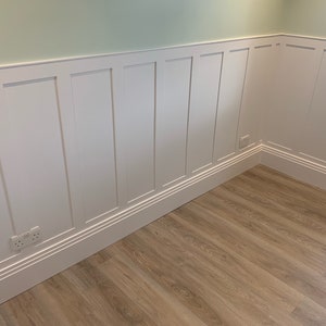 May include: White wainscoting with a light green wall above and a light brown wood floor. The wainscoting has a raised molding around the edges of each panel.