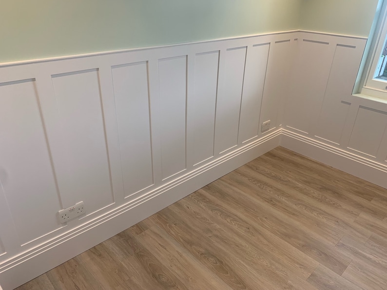 May include: White wainscoting with a light green wall above and a light brown wood floor. The wainscoting has a raised molding around the edges of each panel.