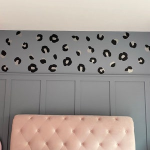 Op de afbeelding: Een roze, gestoffeerde hoofdbord met een grijze muur erachter. De muur is versierd met zwarte en witte luipaardprint stickers.