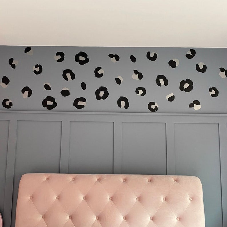 Op de afbeelding: Een roze, gestoffeerde hoofdbord met een grijze muur erachter. De muur is versierd met zwarte en witte luipaardprint stickers.