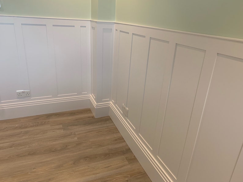 May include: White wainscoting with a raised panel design, featuring a light green wall above and a wood floor below.