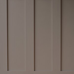 May include: A wall with three vertical panels, each painted a light brown color. The panels are separated by thin white lines.