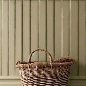 May include: A woven wicker basket with a handle sits in front of a light green vertical panel wall. The basket is filled with dried grasses. The wall and basket create a rustic, farmhouse aesthetic.