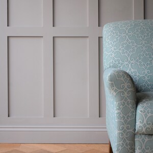 May include: A light blue armchair with a patterned fabric upholstery. The chair is in front of a wall with white wainscoting.
