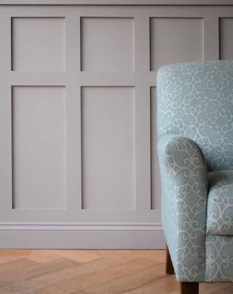 May include: A light blue armchair with a patterned fabric upholstery. The chair is in front of a wall with white wainscoting.