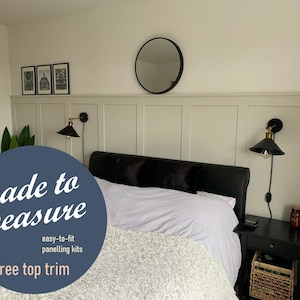 May include: A bedroom with a white bed, black headboard, and white bedding. The wall behind the bed has white wainscoting with a round mirror above it. Two black wall sconces with gold accents are on either side of the bed. The text "made to measure" is in a blue circle with the words "easy-to-fit panelling kits" and "free top trim" below it.
