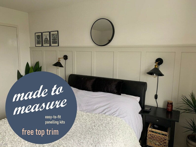 May include: A bedroom with a white bed, black headboard, and white bedding. The wall behind the bed has white wainscoting with a round mirror above it. Two black wall sconces with gold accents are on either side of the bed. The text "made to measure" is in a blue circle with the words "easy-to-fit panelling kits" and "free top trim" below it.