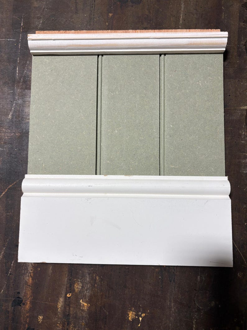 May include: A section of a wall paneling system, featuring a light green vertical panel with white trim at the top and bottom. The top trim includes a natural wood edge. The paneling is designed for interior use.