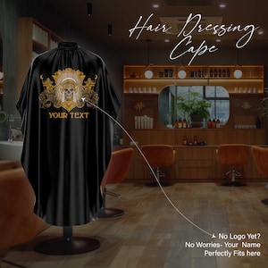 Puede incluir: Capa de peluquería negra con un diseño de tocado nativo americano dorado y beige con una calavera y el texto "YOUR TEXT". La capa se muestra sobre un soporte negro en un salón. Las palabras "Hair Dressing Cape" están escritas en cursiva.