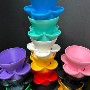 Op de afbeelding: Een stapel kleurrijke, 3D-geprinte, bloemvormige potten. De potten zijn gerangschikt in een regenboogpatroon, beginnend met blauw bovenaan en eindigend met groen onderaan. Elke pot heeft een kleine lip rond de rand en drie kleine gaten aan de onderkant.