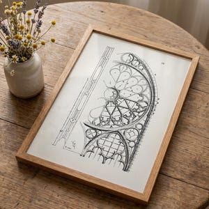 Puede incluir: Un dibujo arquitect&oacute;nico en blanco y negro enmarcado de un dise&ntilde;o de vidriera. El dibujo est&aacute; en un marco de madera marr&oacute;n claro. Un peque&ntilde;o jarr&oacute;n con flores secas se encuentra a la izquierda del marco sobre una mesa de madera.