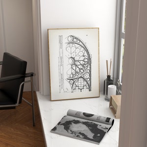 Puede incluir: Un dibujo arquitect&oacute;nico en blanco y negro enmarcado de una ventana de catedral. La obra de arte se muestra sobre una superficie de m&aacute;rmol blanco, junto a una revista enrollada con un dise&ntilde;o de mapa del mundo. Una silla negra es visible.