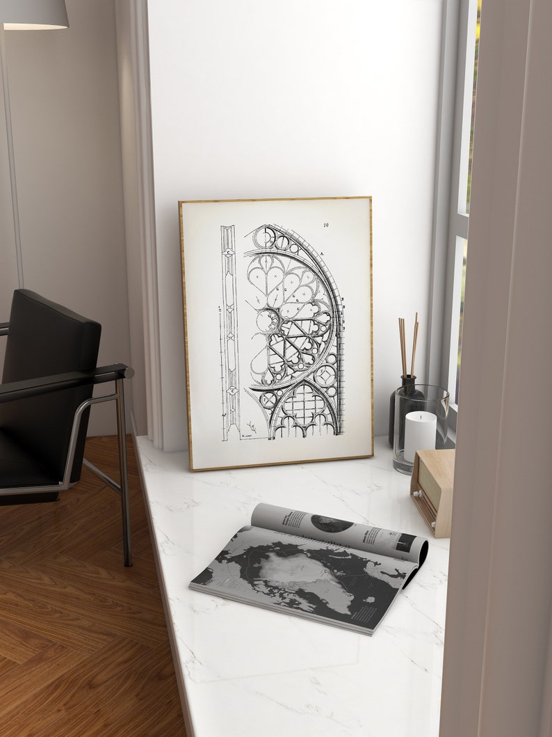 Puede incluir: Un dibujo arquitect&oacute;nico en blanco y negro enmarcado de una ventana de catedral. La obra de arte se muestra sobre una superficie de m&aacute;rmol blanco, junto a una revista enrollada con un dise&ntilde;o de mapa del mundo. Una silla negra es visible.
