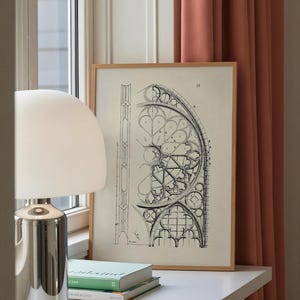 Puede incluir: Un dibujo arquitect&oacute;nico enmarcado con un marco de madera clara. El dibujo en blanco y negro representa una secci&oacute;n de un dise&ntilde;o de vidriera. Una l&aacute;mpara plateada y dos libros est&aacute;n sobre una superficie blanca.