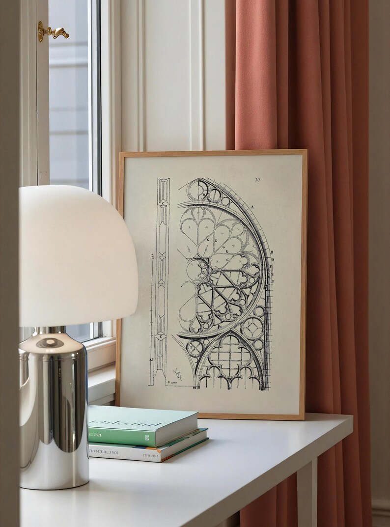Puede incluir: Un dibujo arquitect&oacute;nico enmarcado con un marco de madera clara. El dibujo en blanco y negro representa una secci&oacute;n de un dise&ntilde;o de vidriera. Una l&aacute;mpara plateada y dos libros est&aacute;n sobre una superficie blanca.