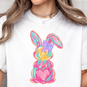 May include: White t-shirt featuring a colourful abstract bunny design. The bunny has a pink heart and a purple bow.