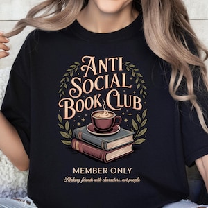 May include: Black t-shirt featuring the words "Anti Social Book Club" in a decorative font, with an illustration of a coffee cup on books. The text "Member Only" and "Making friends with characters, not people" are also included.