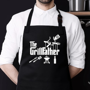Peut inclure: Tablier noir avec du texte blanc qui dit "The Grillfather" et un graphique d'outils de grillade.