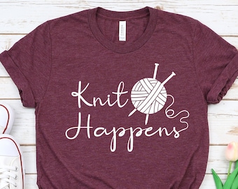 May include: A maroon t-shirt with the text "Knit Happens" in white lettering. A white yarn ball with knitting needles is pictured next to the text.