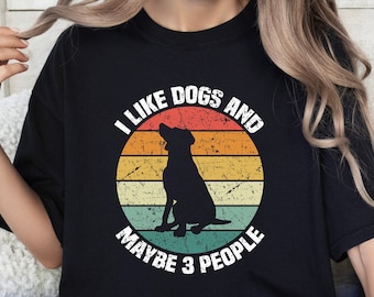 Könnte beinhalten: Ein schwarzes T-Shirt mit einer Grafik im Vintage-Stil, auf dem "Ich mag Hunde und vielleicht 3 Leute" steht. Die Grafik zeigt eine Silhouette eines Hundes, der vor einem Sonnenuntergang sitzt.