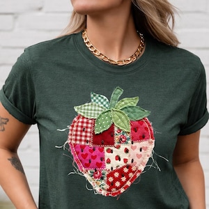 May include: Dark green t-shirt with a patchwork strawberry motif. The strawberry design incorporates diverse fabric patterns, such as gingham, floral, and heart prints. The shirt has rolled sleeves and a round neckline.