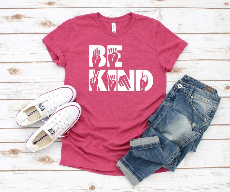 May include: A pink t-shirt with the words "BE KIND" in white lettering. The letters are formed using American Sign Language hand gestures.