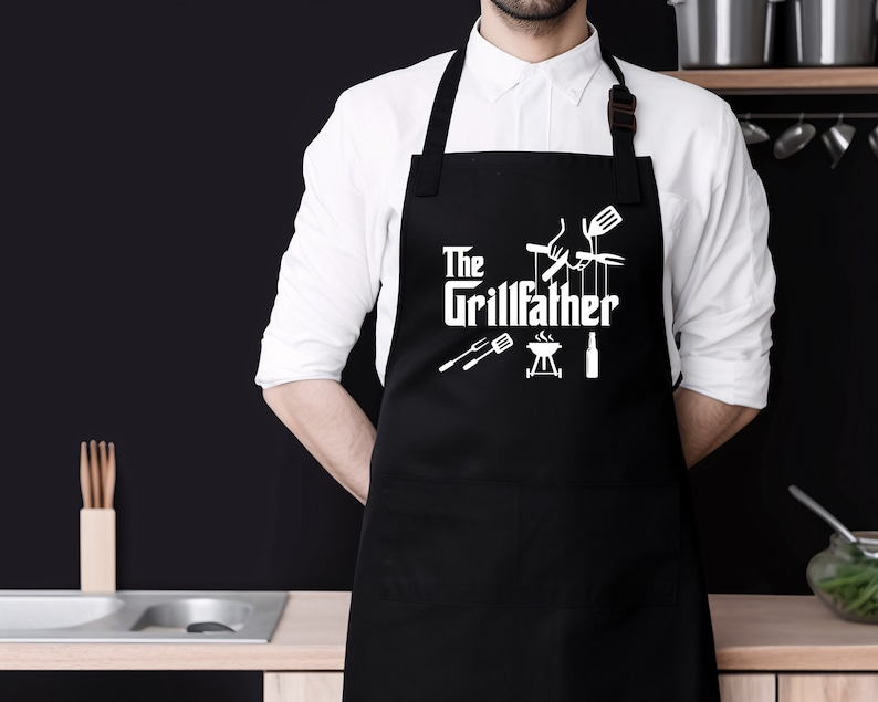 Peut inclure: Tablier noir avec du texte blanc qui dit "The Grillfather" et un graphique d'outils de grillade.
