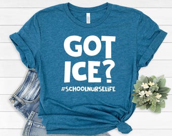 Puede incluir: Una camiseta de color azul cerceta jaspeado con el texto blanco GOT ICE? y el hashtag #SCHOOLNURSELIFE impresos en una fuente negrita sin remates en el pecho. La prenda tiene mangas cortas y un cuello redondo clásico.