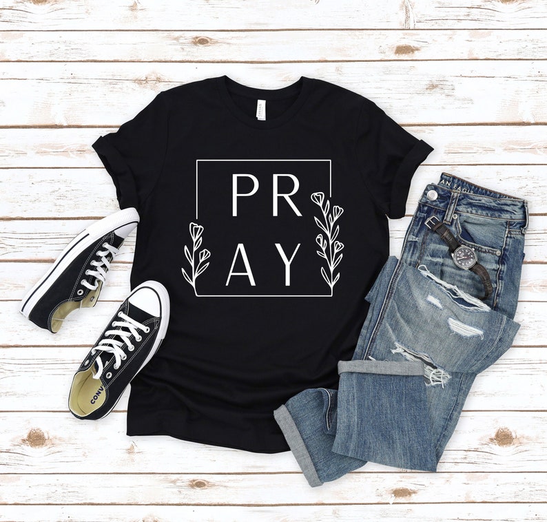 May include: Black t-shirt with white text that says "PRAY" inside a square with floral accents.