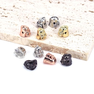 May include: A collection of nine metal charms in various finishes, including silver, gold, and black. Each charm features a detailed design of a helmet, possibly inspired by a popular science fiction character.