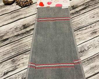 May include: Gray kitchen towel with red and white embroidered stripes. The top portion features a white fabric with red and pink hearts. The towel has a loop for hanging.