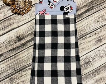 May include: Black and white checkered kitchen towel with a blue and white fabric loop featuring Mickey Mouse and Minnie Mouse characters. The loop has the text "Kitchen Goods" printed on it.