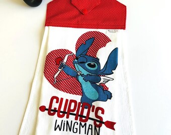 May include: White kitchen towel with a red heart and a blue Stitch character holding an arrow. The text "Cupid's Wingman" is printed below the character.
