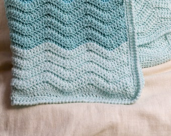 May include: A crocheted baby blanket with a wavy pattern in shades of blue and green.