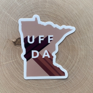 May include: A sticker of the state of Minnesota with the words "UFF DA" in white letters on a brown background.