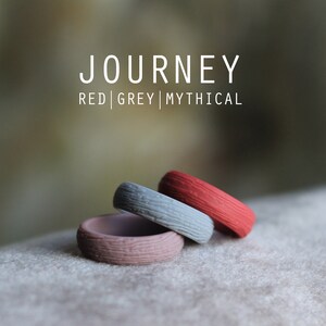 May include: Three silicone rings stacked on top of each other. The top ring is red, the middle ring is gray, and the bottom ring is a light brown color. The rings have a textured surface and the text "JOURNEY RED | GREY | MYTHICAL" is visible above the rings.