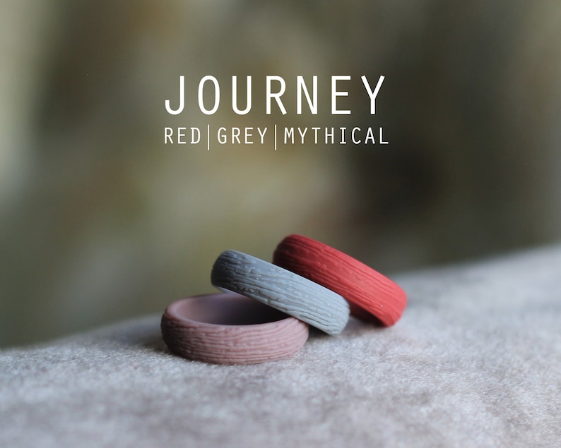 May include: Three silicone rings stacked on top of each other. The top ring is red, the middle ring is gray, and the bottom ring is a light brown color. The rings have a textured surface and the text "JOURNEY RED | GREY | MYTHICAL" is visible above the rings.