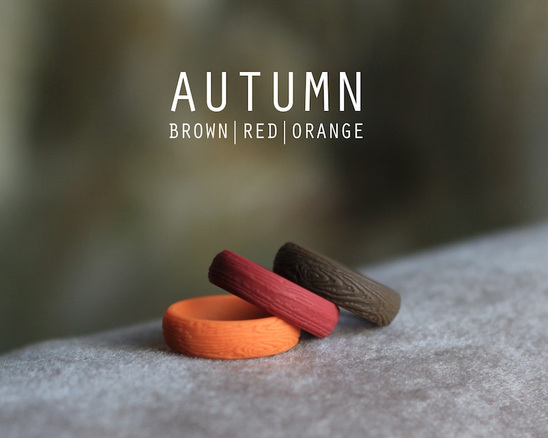 May include: Three silicone rings in brown, red, and orange with a wood grain pattern. The rings are stacked on top of each other. The text "AUTUMN BROWN | RED | ORANGE" is above the rings.