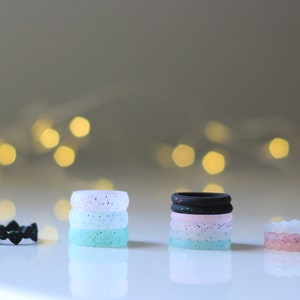 Pode incluir: Um conjunto de cinco an&eacute;is de silicone empilhados uns sobre os outros. Os an&eacute;is s&atilde;o de diferentes cores e padr&otilde;es, incluindo preto, rosa, branco e azul. Os an&eacute;is s&atilde;o todos feitos de silicone e s&atilde;o projetados para serem confort&aacute;veis de usar.