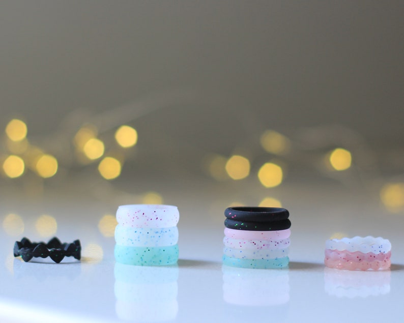 Pode incluir: Um conjunto de cinco an&eacute;is de silicone empilhados uns sobre os outros. Os an&eacute;is s&atilde;o de diferentes cores e padr&otilde;es, incluindo preto, rosa, branco e azul. Os an&eacute;is s&atilde;o todos feitos de silicone e s&atilde;o projetados para serem confort&aacute;veis de usar.