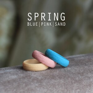 May include: Three silicone rings stacked on top of each other. The top ring is blue, the middle ring is pink, and the bottom ring is a light beige color. The rings are labeled "SPRING BLUE | PINK | SAND".