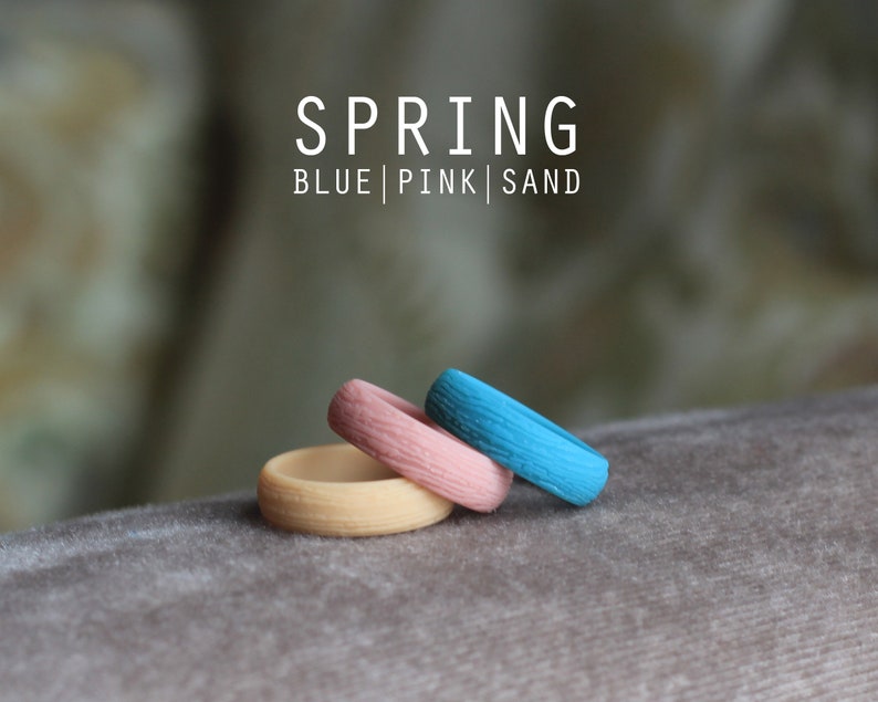 May include: Three silicone rings stacked on top of each other. The top ring is blue, the middle ring is pink, and the bottom ring is a light beige color. The rings are labeled "SPRING BLUE | PINK | SAND".
