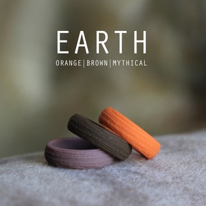 May include: Three stacked silicone rings in orange, brown, and purple. The rings have a textured surface and are labeled "EARTH | ORANGE | BROWN | MYTHICAL".