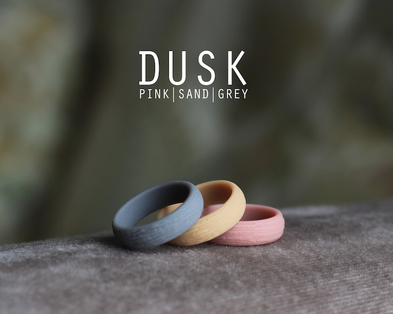 May include: Three silicone rings in pink, sand, and gray colors. The rings are stacked on top of each other. The text "DUSK PINK | SAND | GREY" is displayed above the rings.