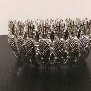 May include: Silver bracelet featuring a pineapple design. The bracelet is made of metal and has a shiny finish.