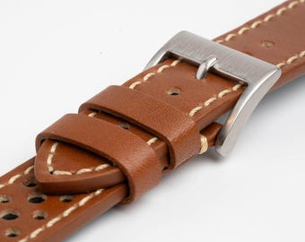 May include: A tan leather watch strap featuring a series of small circular perforations along the length, accented with light-colored contrast stitching and a brushed silver-tone metal pin buckle with two matching leather keepers.