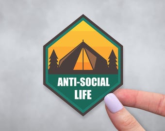 May include: A green and yellow hexagonal sticker with a silhouette of a tent, trees, and the text "ANTI-SOCIAL LIFE".