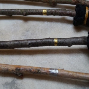 May include: Three wooden sticks with black fabric wrapped around the ends and gold tape accents. The sticks are arranged in a row on a light beige surface.