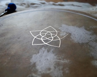 May include: A close-up of a brown leather drum with a white geometric design in the center. The design is a five-pointed star with overlapping circles.